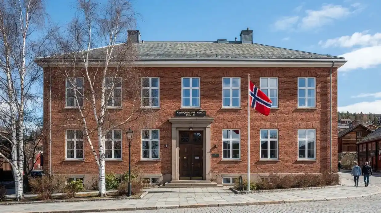 Offentlig kontorbygning i rødt murstein i en norsk by, med et flagg ved inngangen og blå himmel